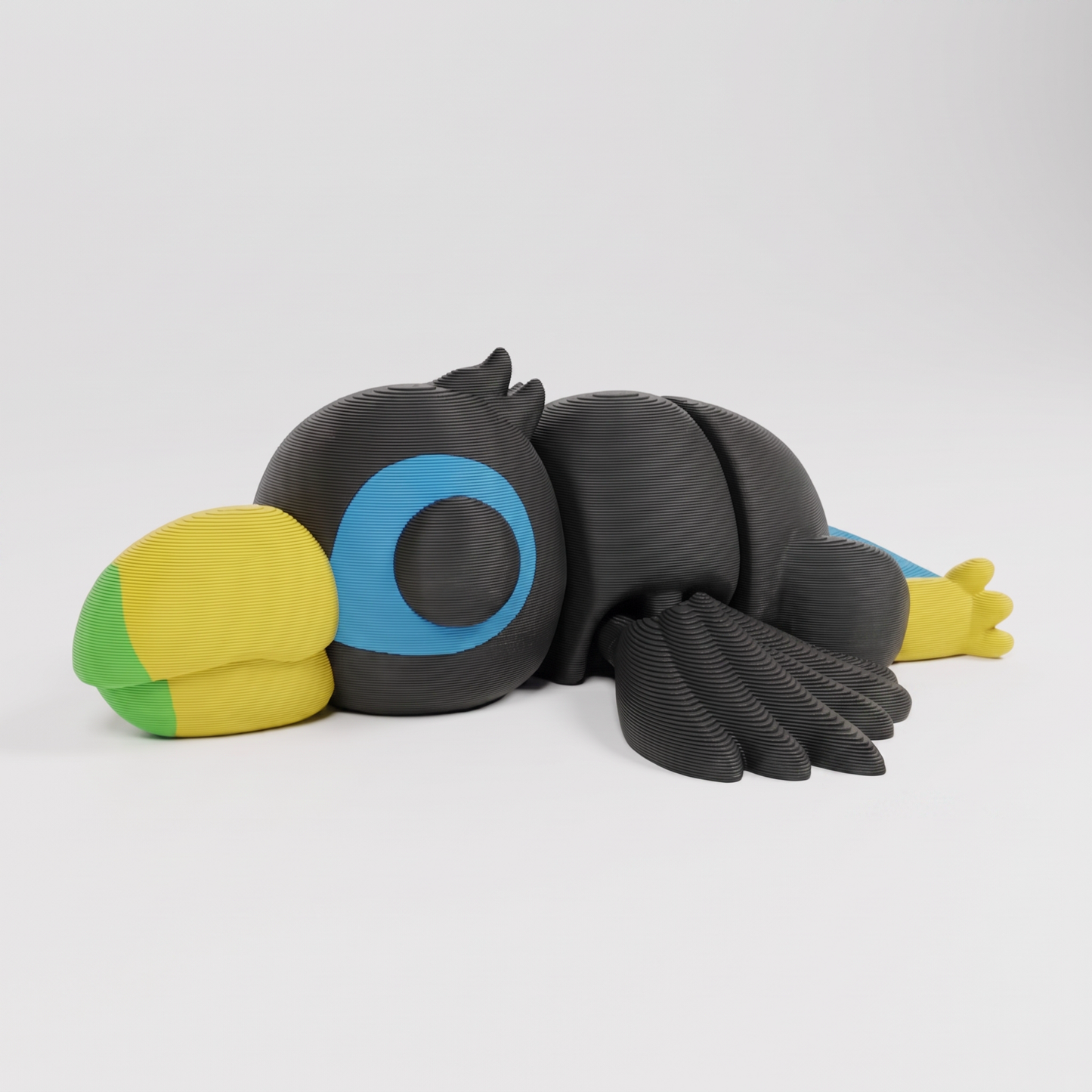 Figura decorativa articulada de tucán en gris oscuro, verde, amarillo y azul sobre fondo perla