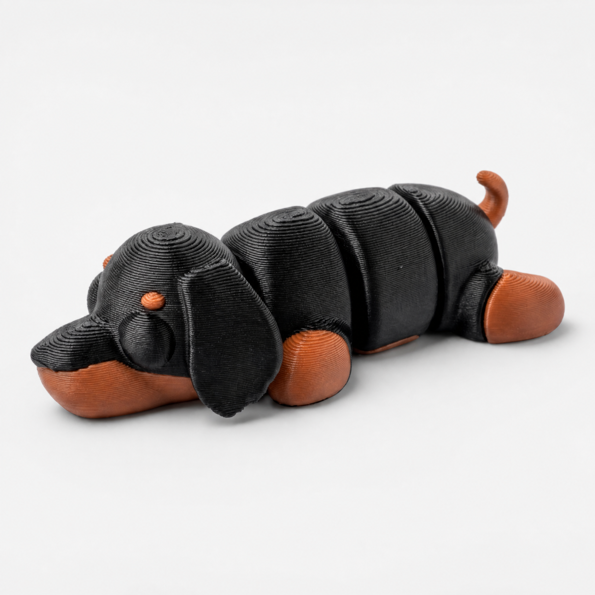 Figura decorativa articulada de perro salchicha en marrón terracota y negro sobre fondo perla